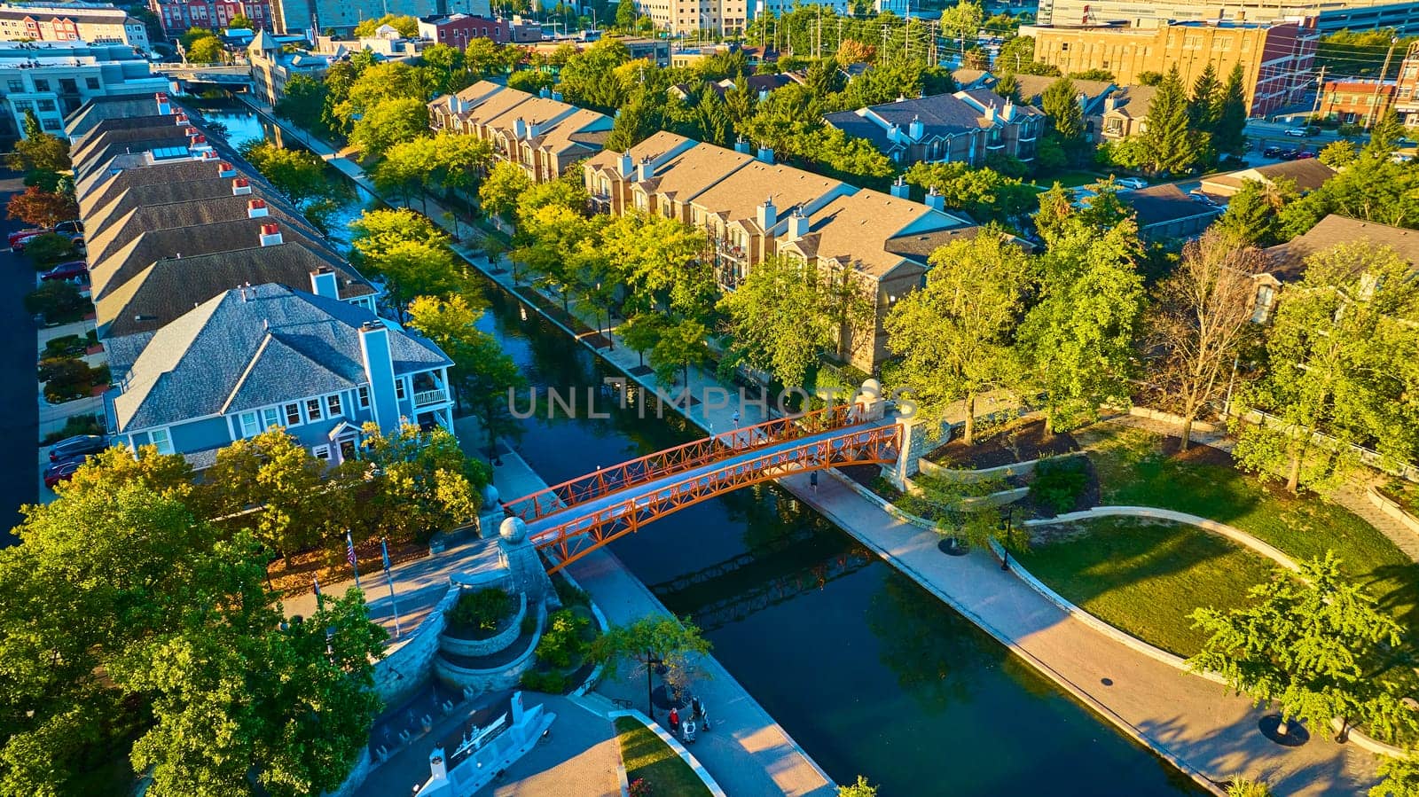 Golden Hour Over Indianapolis Canal: an Aerial View of a Red Pedestrian Bridge, Gabled Townhouses, and Tranquil Waters