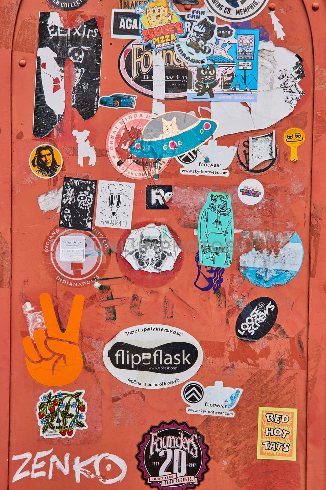 Vibrant collage of diverse stickers on red metal surface, showcasing urban street art and culture in downtown Muncie, Indiana, 2023