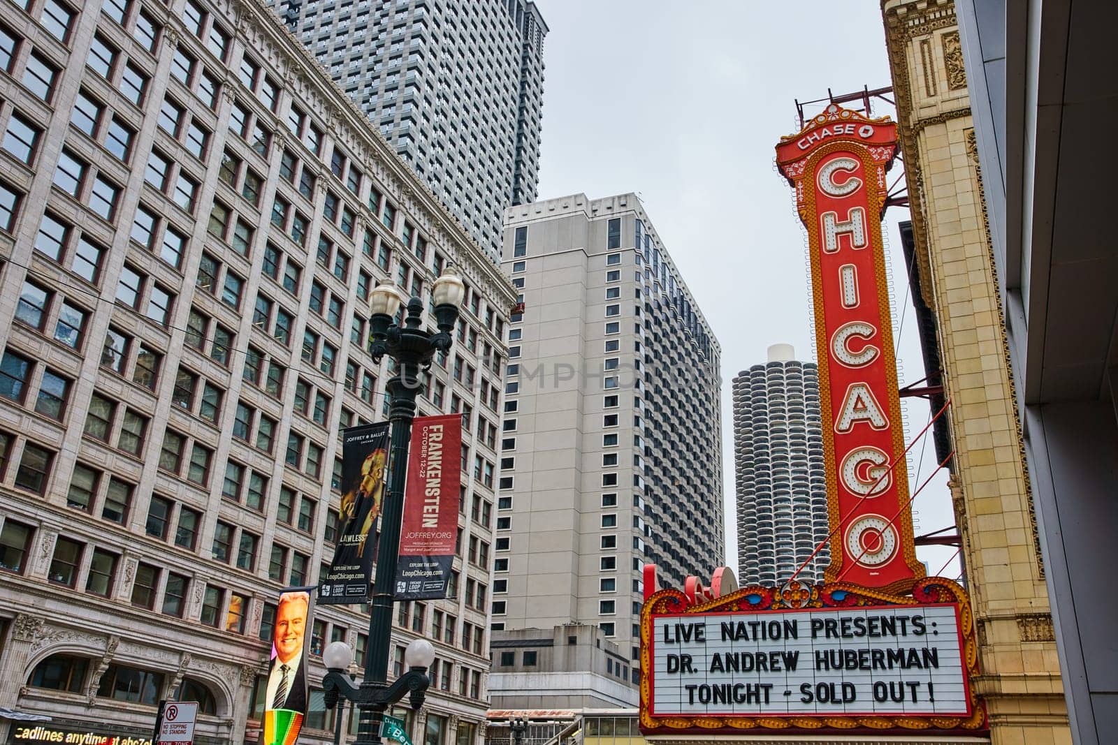 Image of Large orange sign with Chicago in white lettering above a theatre sign in city with skyscrapers