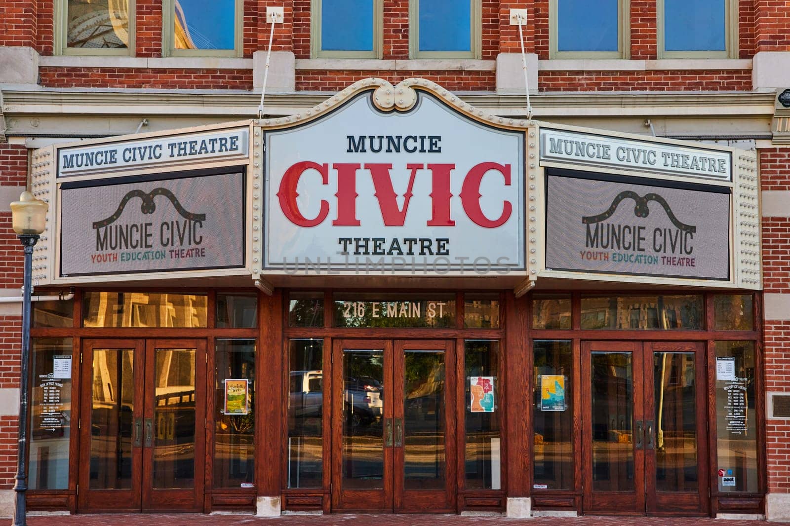 Daytime view of Muncie Civic Theatre's traditional red brick facade, detailed marquee signs highlighting youth education, and elegant entrance at 216 E Main St, Downtown Indiana, 2023