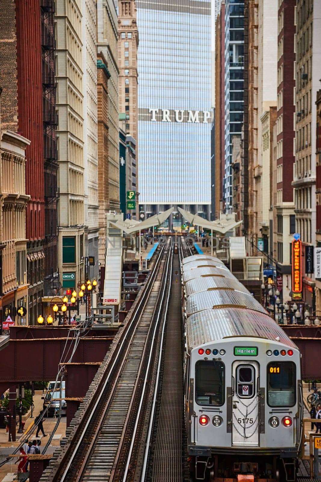 Silver Harlem Train 011 traversing on elevated tracks through a bustling cityscape, showcasing architectural diversity and the rhythm of urban life in Chicago, Illinois, 2023.