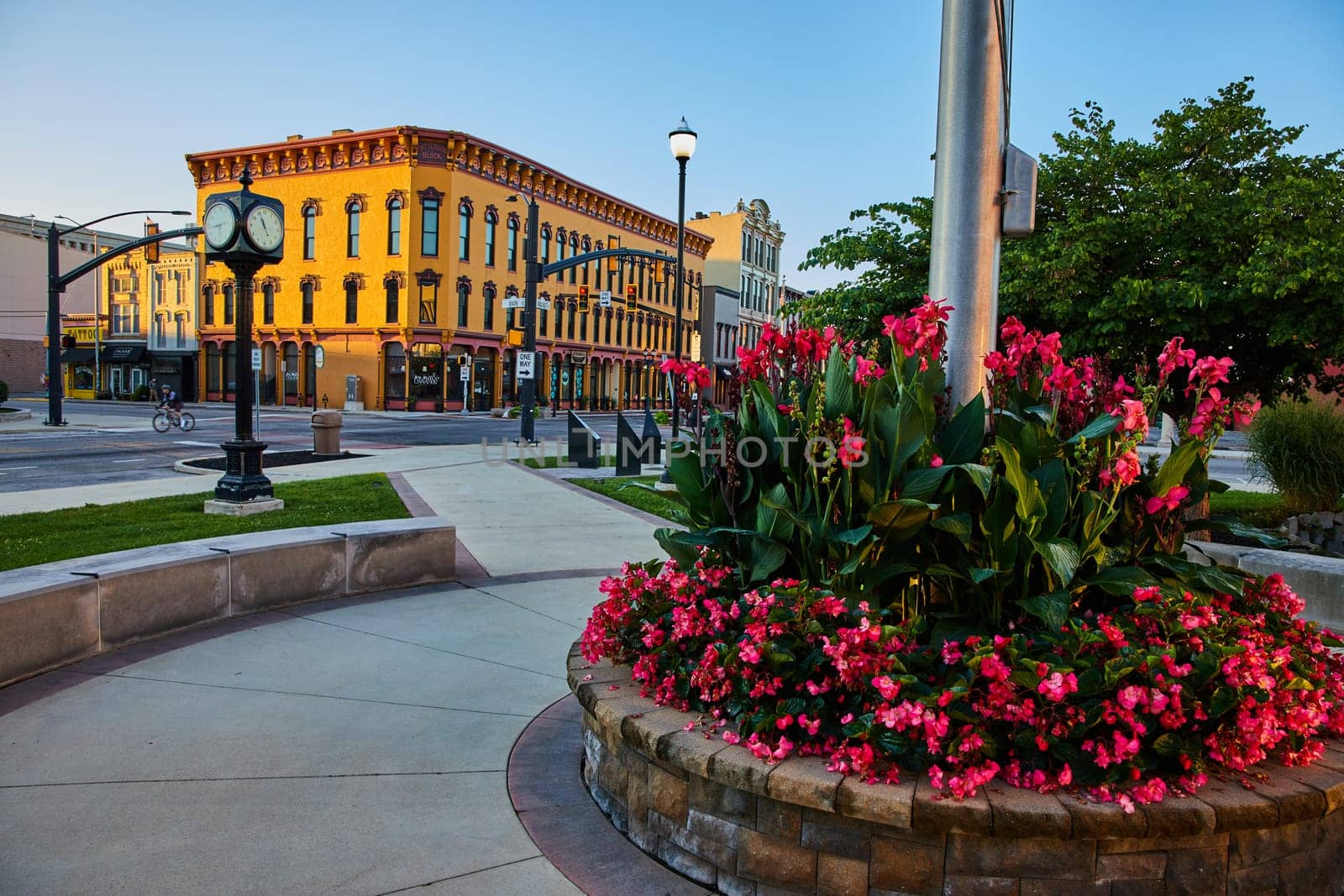Golden hour sunrise over Muncie, Indiana in 2023, showcasing a vibrant cityscape with a blossoming flower bed, a classic street clock, and ornate buildings.
