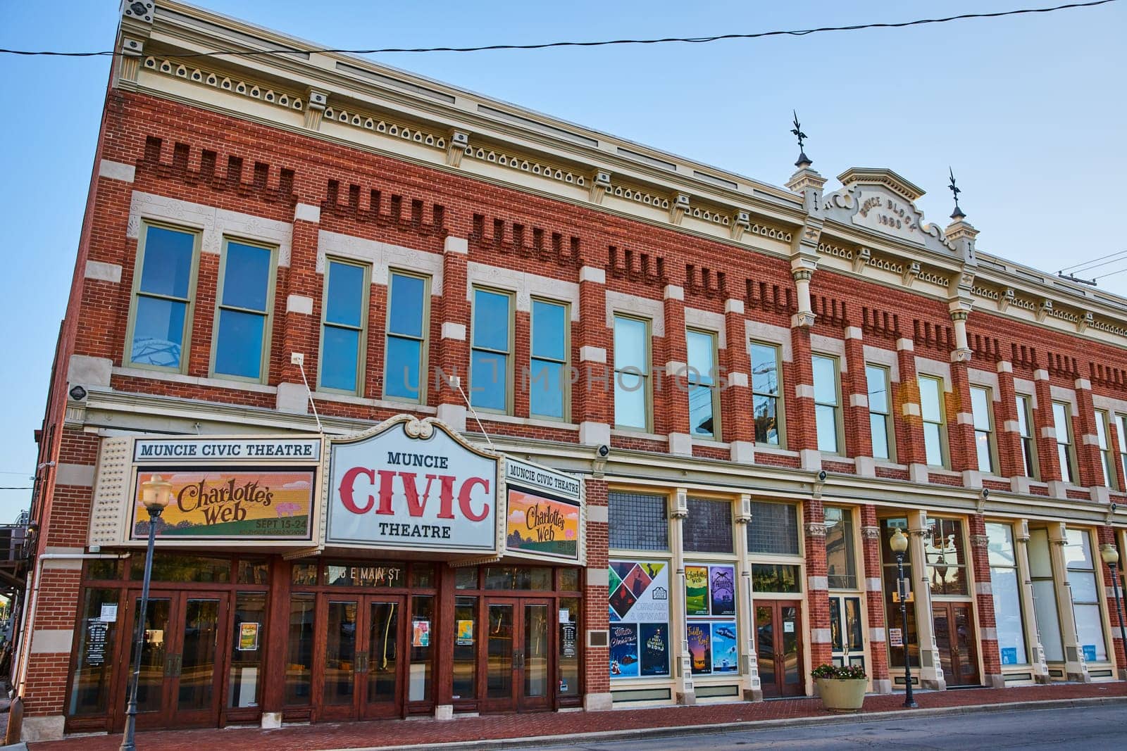 1890 Muncie Civic Theatre, a red brick historic building in downtown Indiana, bathed in daylight, advertising a Charlotte's Web production.