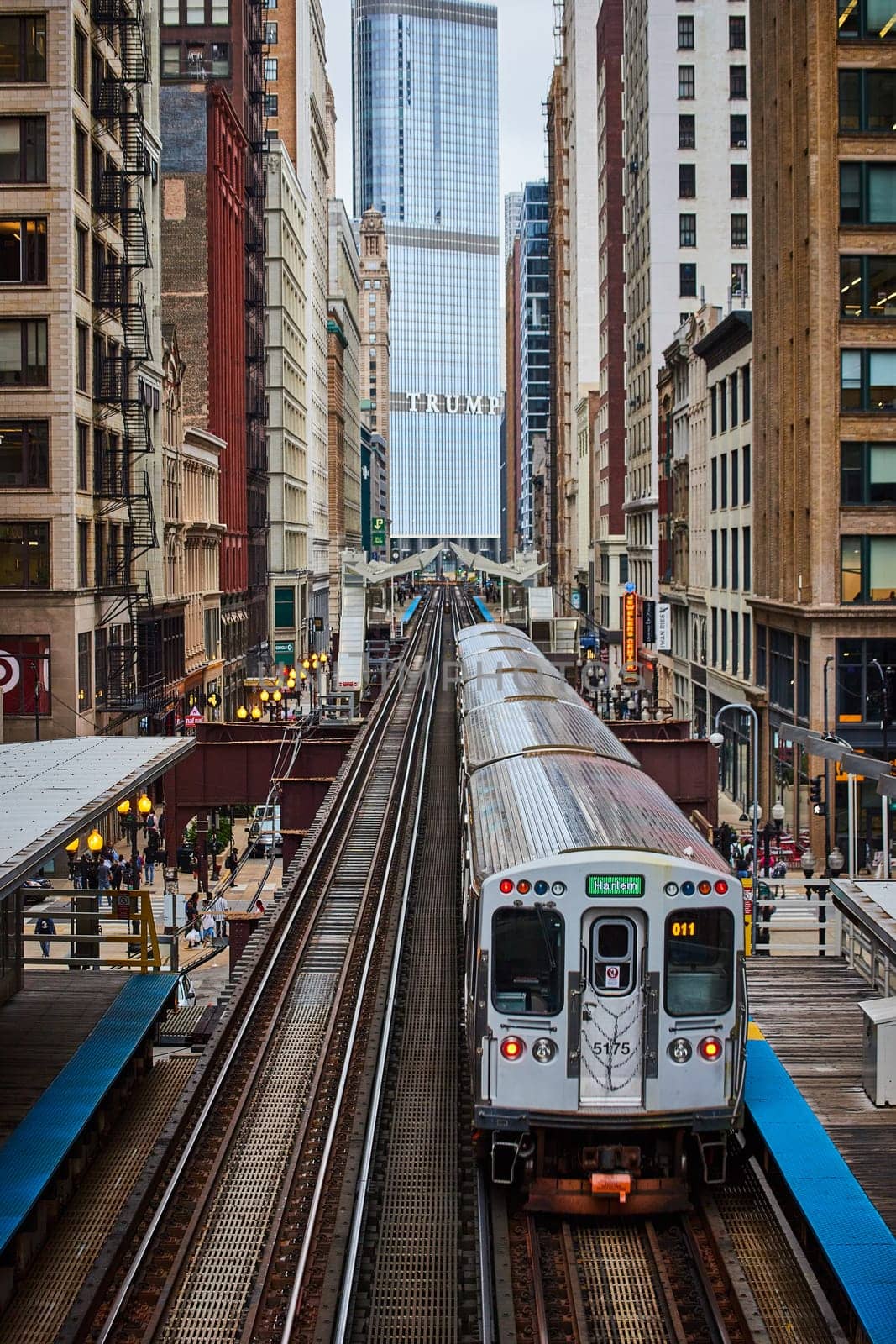 Daytime view of a sleek public transit train marked Harlem, ready on tracks amidst the diverse architecture of urban Chicago, 2023