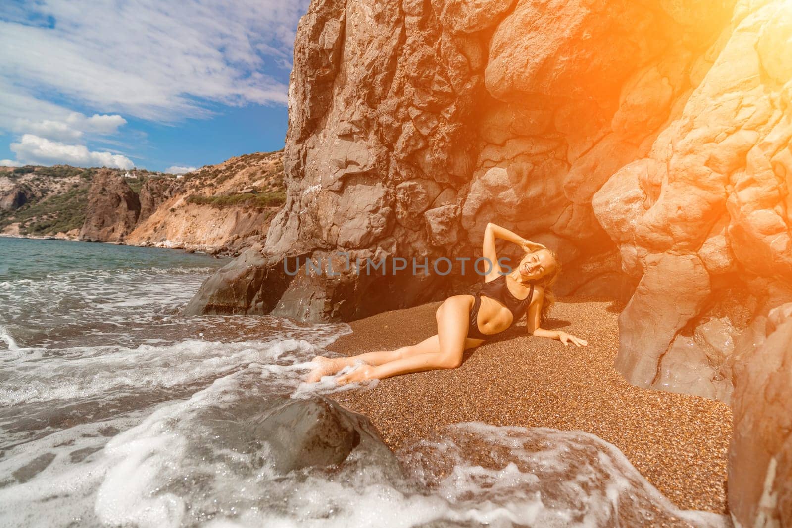 Woman swimsuit sea. Attractive blonde woman in a black swimsuit enjoying the sea air on the seashore around the rocks. Travel and vacation concept. by Matiunina