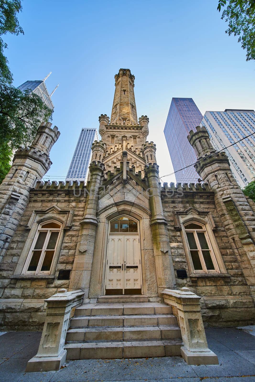 Chicago Water Tower front with lit tower and bright skyscrapers behind framed by lush green trees by njproductions