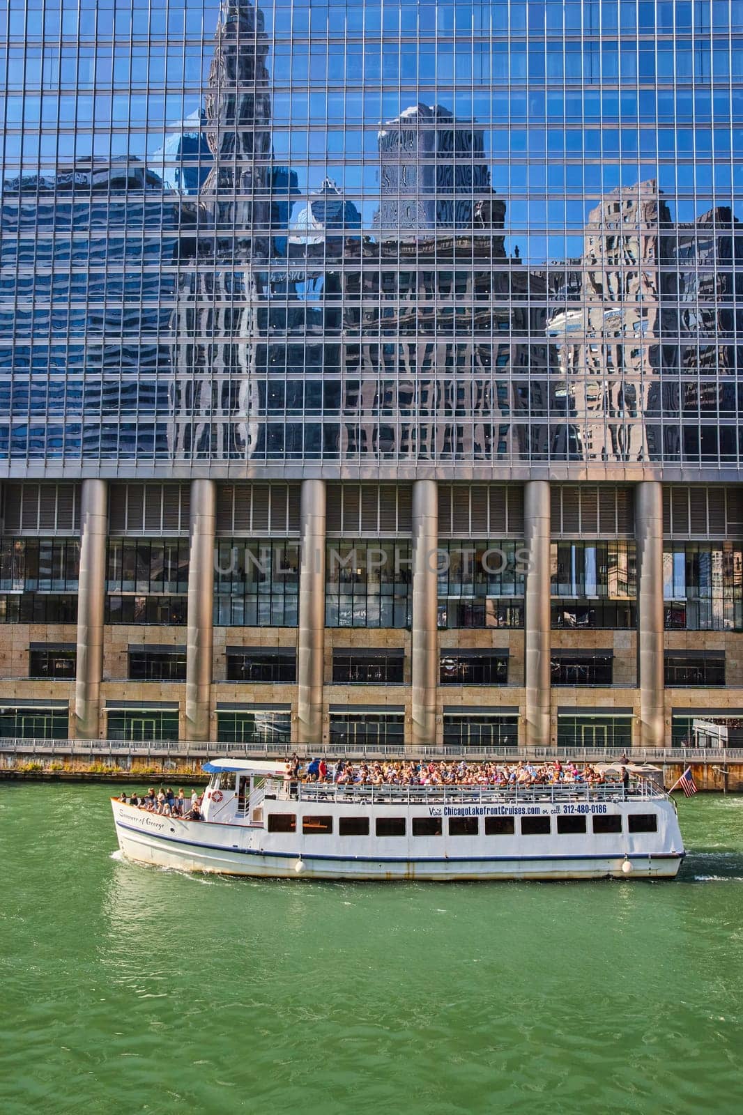 Tourist cruise tour boat on Chicago canal with reflective building showing blue sky and skyscrapers by njproductions