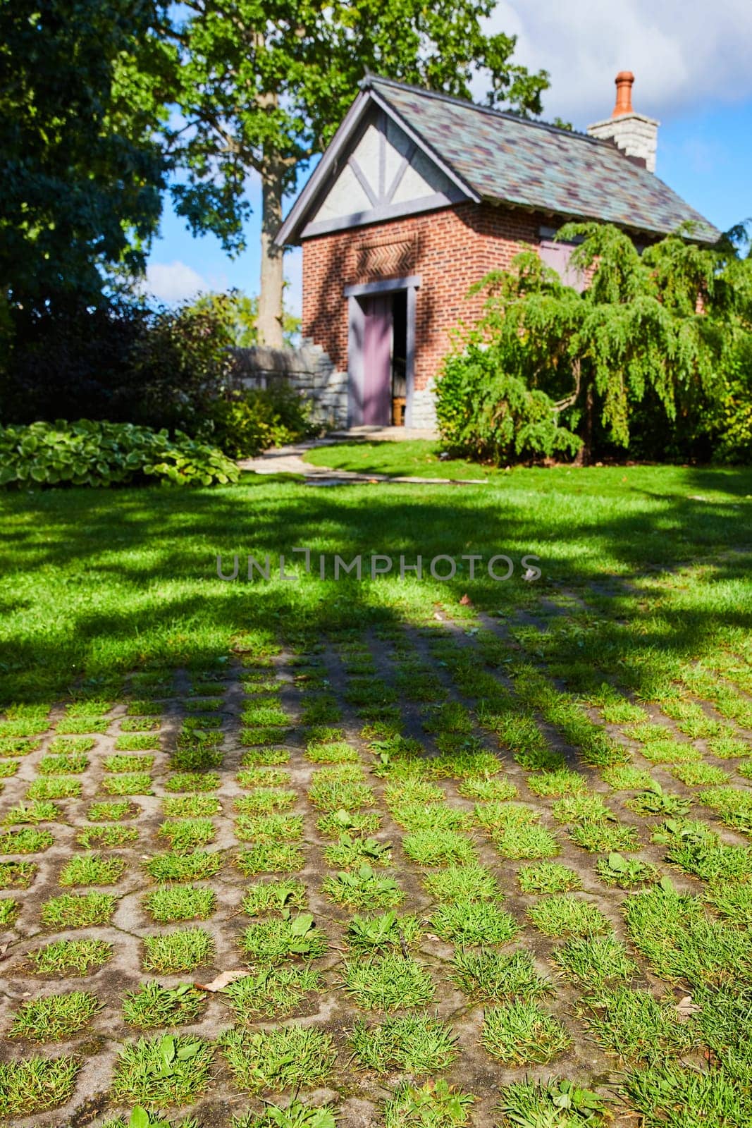 Charming historic brick cottage with purple door nestled in sunlit Botanic Gardens, Elkhart, Indiana, offering a serene retreat