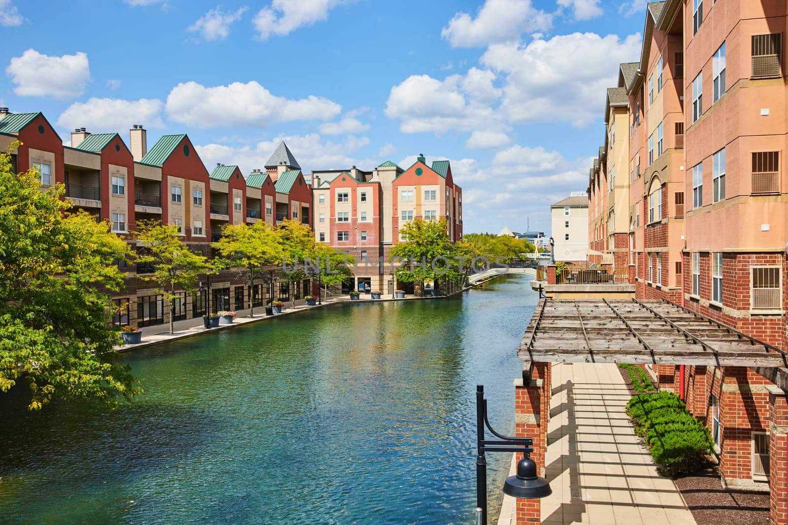 Daytime shot of modern yet quaint canal-side living in Indianapolis, 2023, featuring colorful residential buildings with commercial spaces, and peaceful waterfront ambiance.