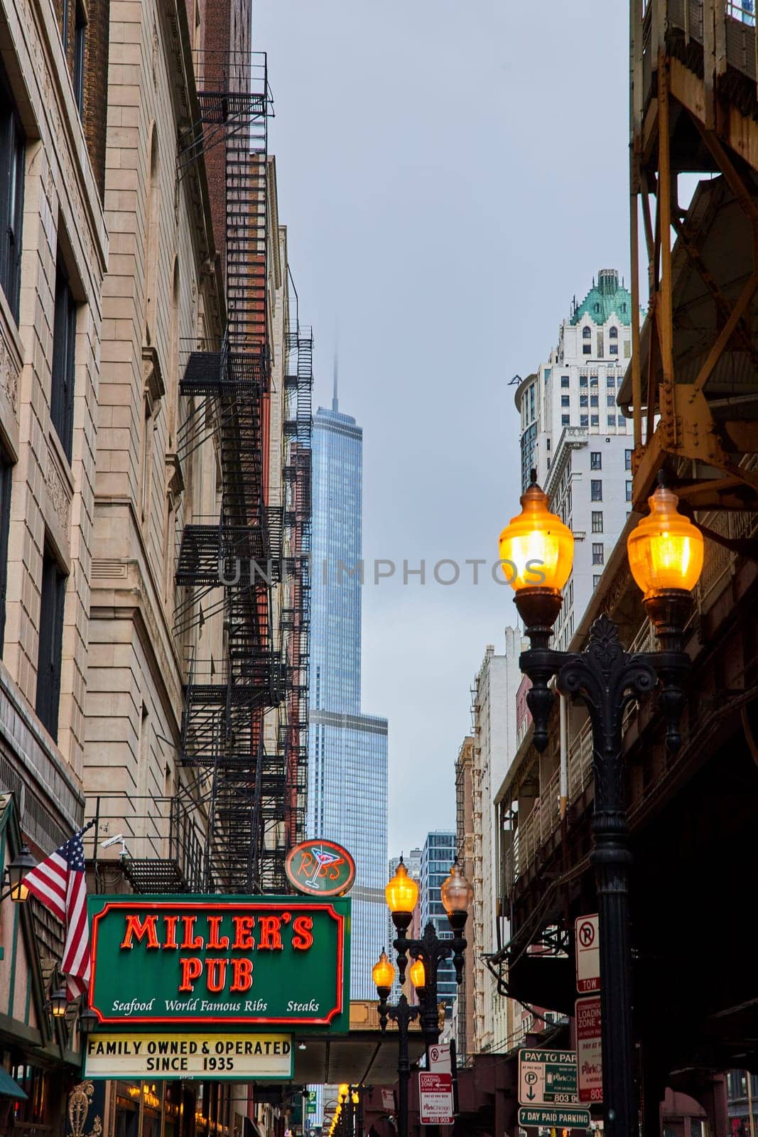 Gloomy Chicago Illinois yellow street lights beside pub family owned sign and skyscrapers, USA by njproductions