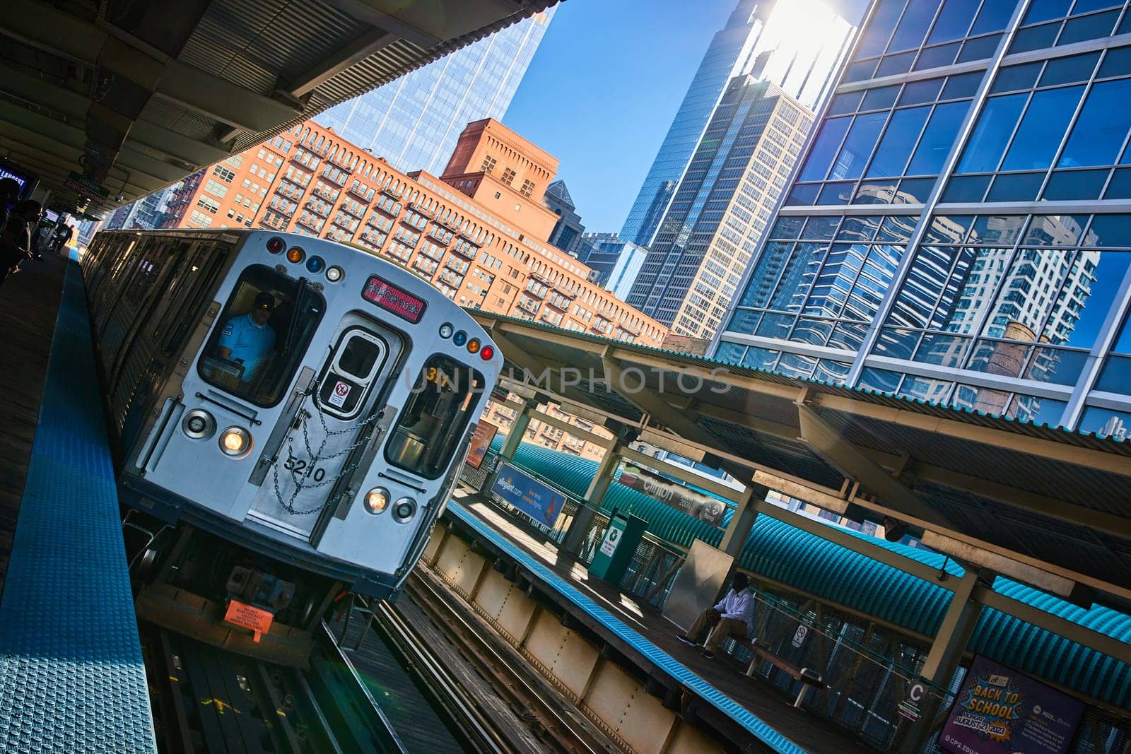 Daylight view of a blue and white striped train on elevated tracks in downtown Chicago, Illinois, 2023, emphasizing urban transportation and architectural contrast.