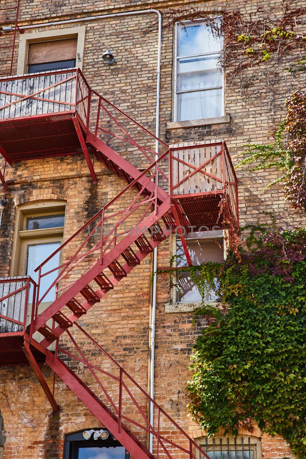 2023 view of a rustic brick building with a red fire escape and climbing ivy in Downtown Elkhart, Indiana showing urban resilience over time.