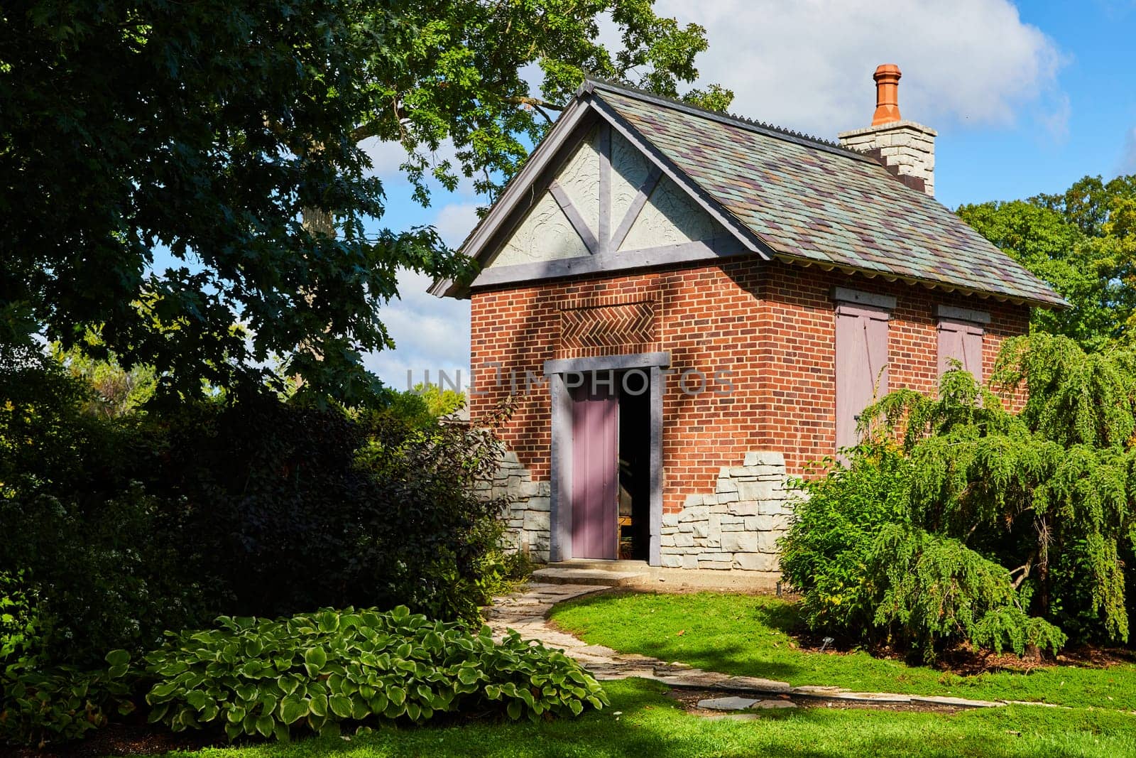 Charming brick cottage amid lush Botanic Gardens in Elkhart, Indiana, 2023, featuring a rustic stone chimney and inviting purple door