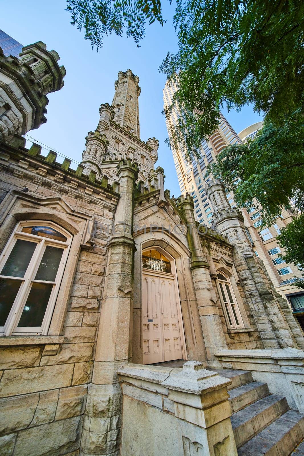 Image of Entrance and tower of Chicago water tower with lush green tree, tourism of city, historic attraction