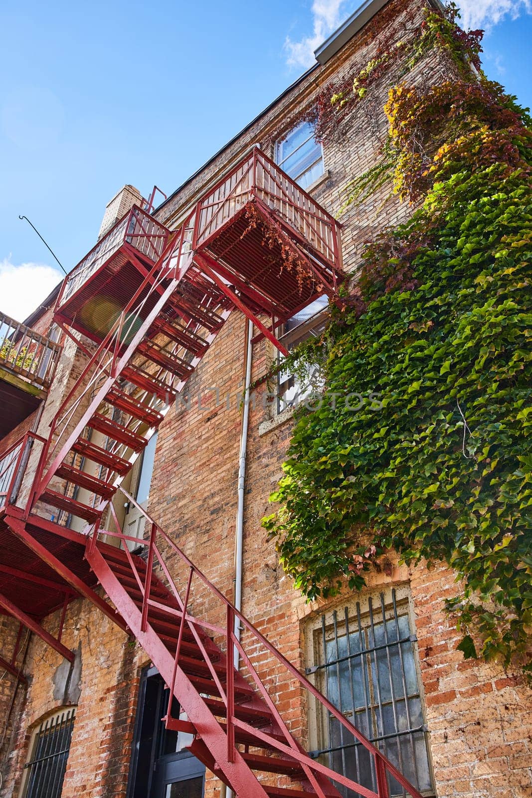 Sunlit Ivy-Covered Historic Brick Building with Striking Red Fire Escape in Downtown Elkhart, Indiana