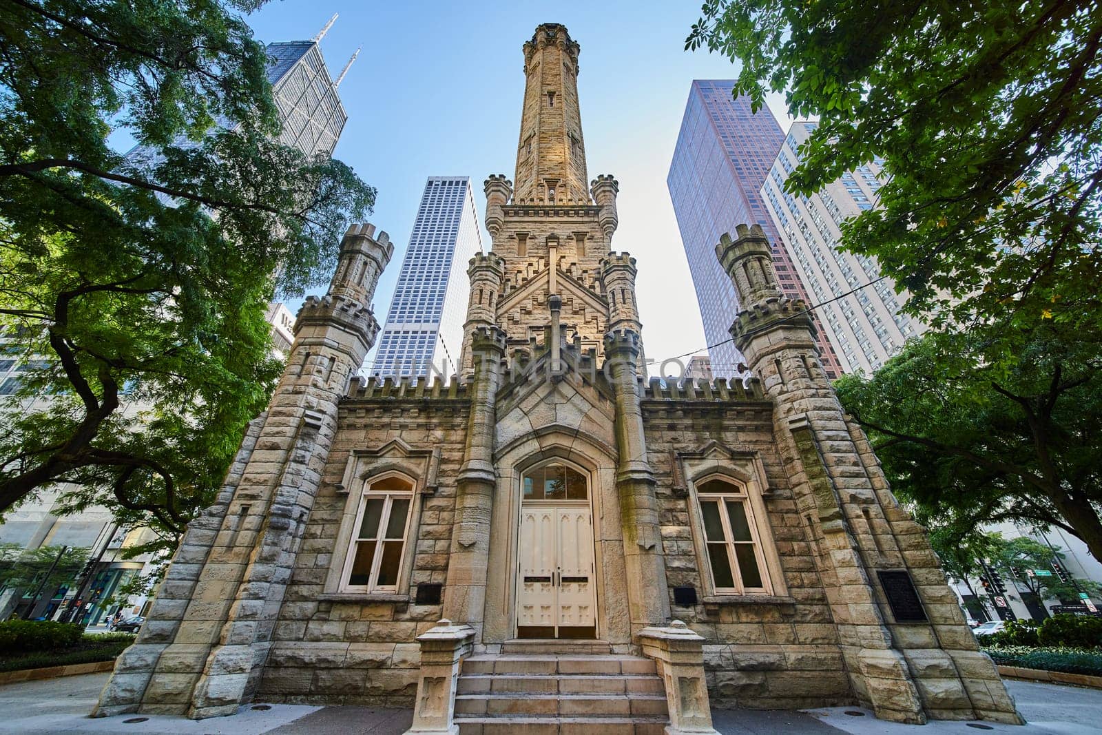 Chicago Water Tower front entrance with lit tower and bright skyscrapers behind framed by lush trees by njproductions
