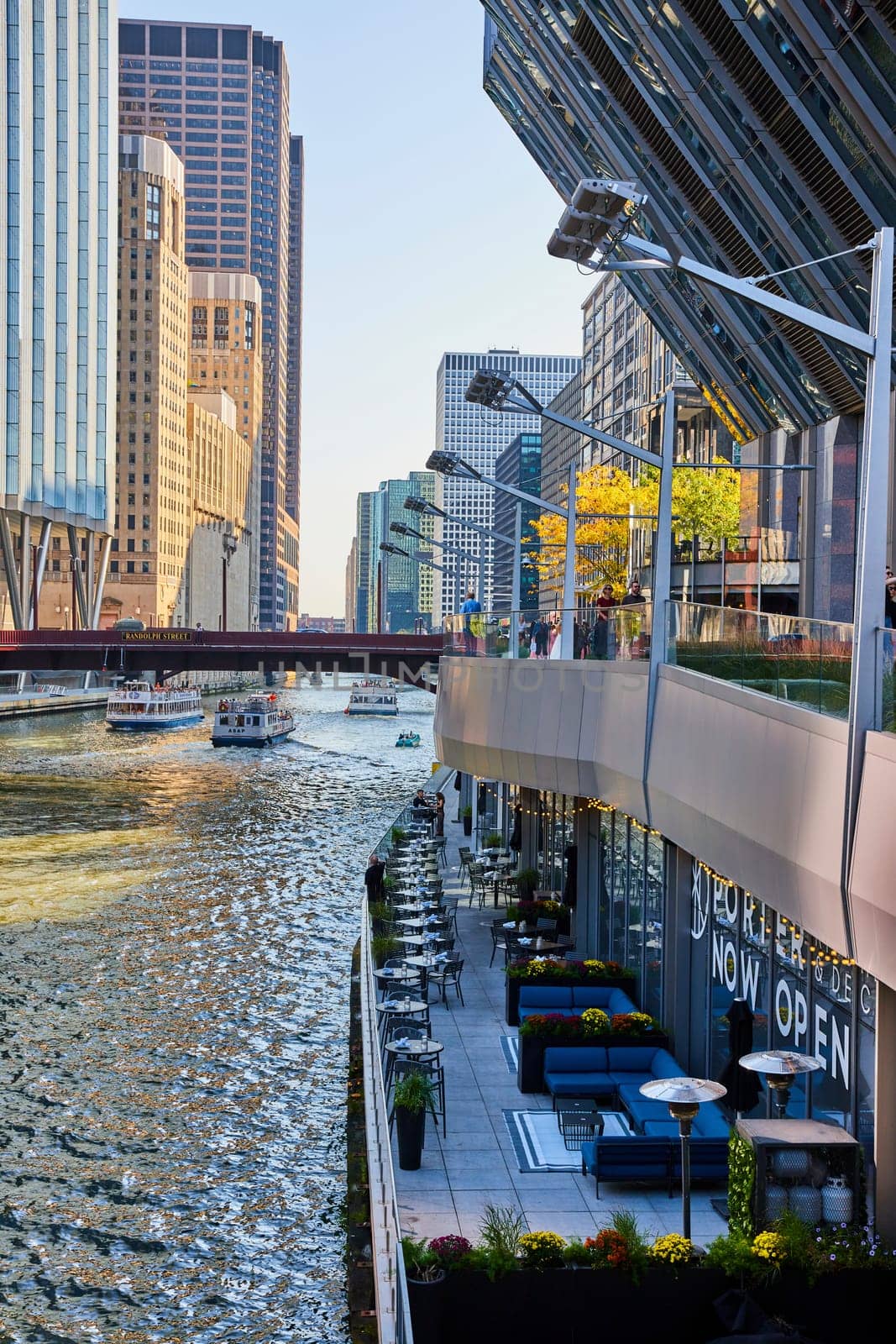 Waterside patio on Chicago canal with tour boats passing under bridge with line of skyscrapers by njproductions