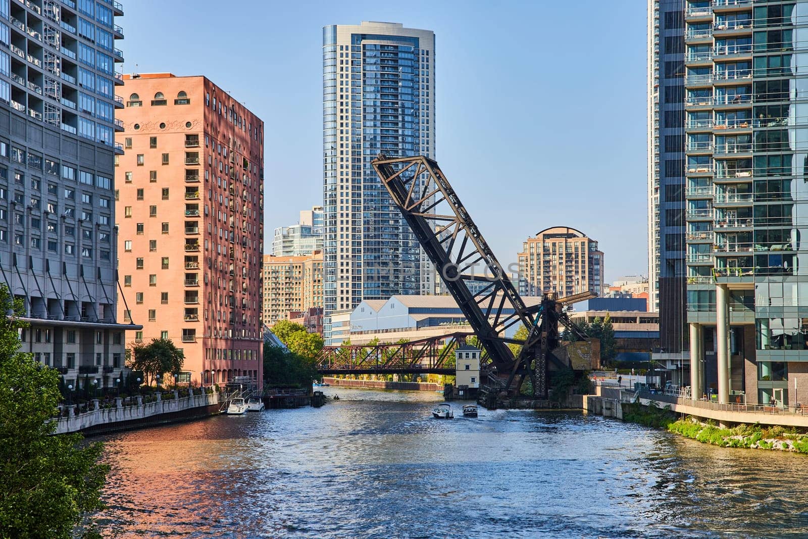 Image of Vertical lift bridge raised over two boats on Chicago canal with skyscrapers on sunny summer day