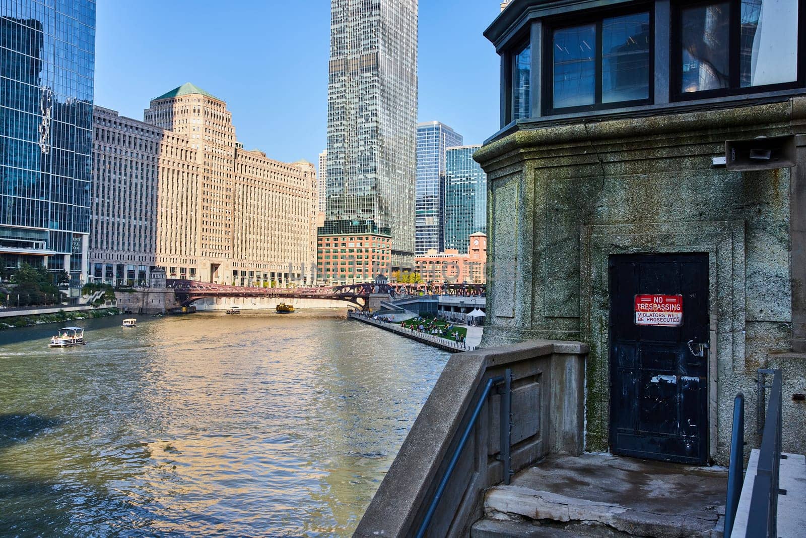 Image of No trespassing door on castle like tower overlooking Chicago canal with boats on water on sunny day