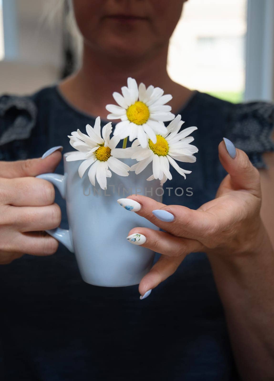 a young woman holds a blue cup of daisies, a beautiful summer manicure by KaterinaDalemans