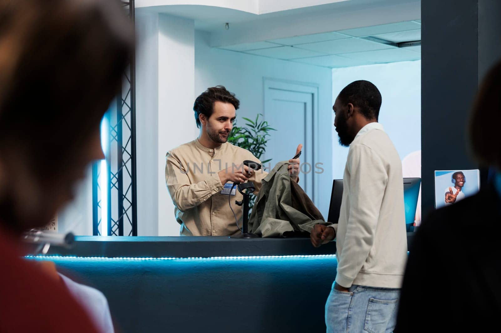 Cashier scanning apparel items for customer at clothing store counter. African american man talking with fashion boutique employee while buying shirt and waiting at cash register