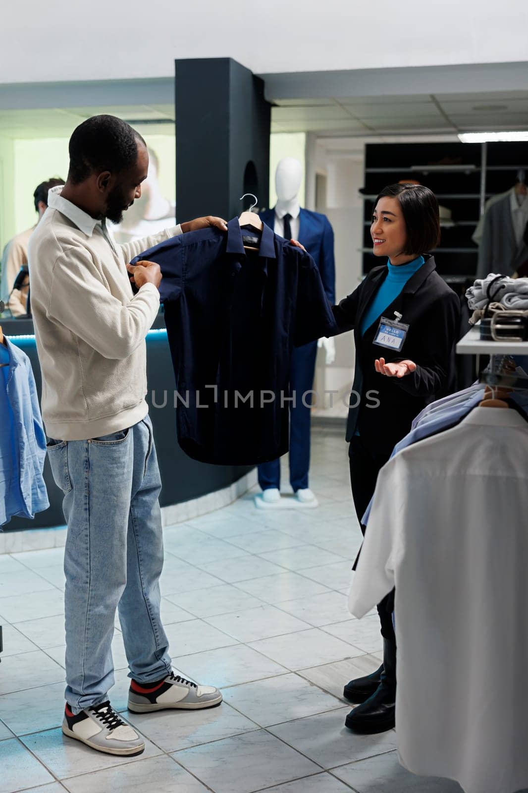 Clothing store assistant offering customer advice in choosing formal shirt. African american man and boutique worker holding formal wear on hanger, examining style before making purchase