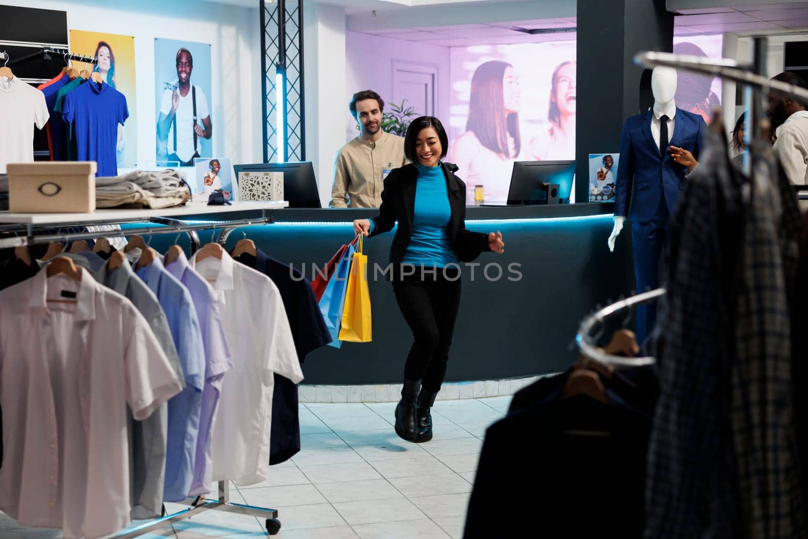 Happy asian shopper carrying packages filled with purchased clothes in department mall boutique. Excited young smiling woman holding paper bags, dancing and enjoying shopping