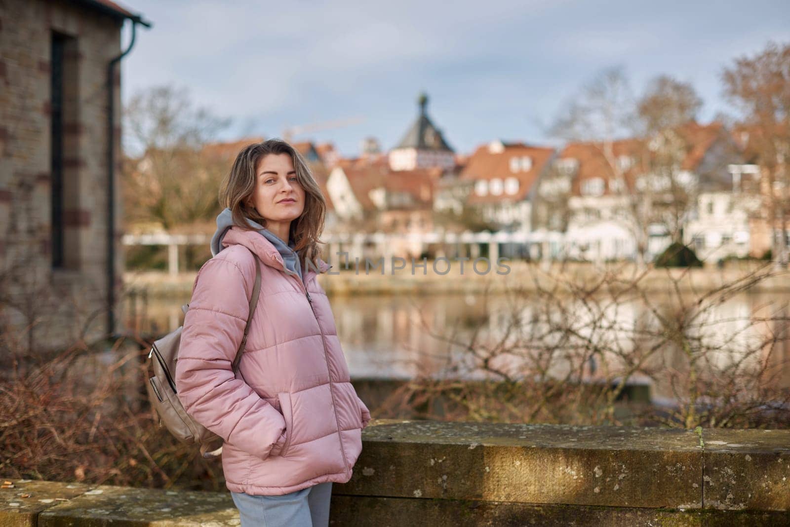 Young beautiful pretty tourist girl in warm hat and coat with backpack walking at cold autumn in Europe city enjoying her travel in Bietigheim-Bissingen, Deutschland. Outdoor portrait of young tourist woman enjoying sightseeing by Andrii_Ko