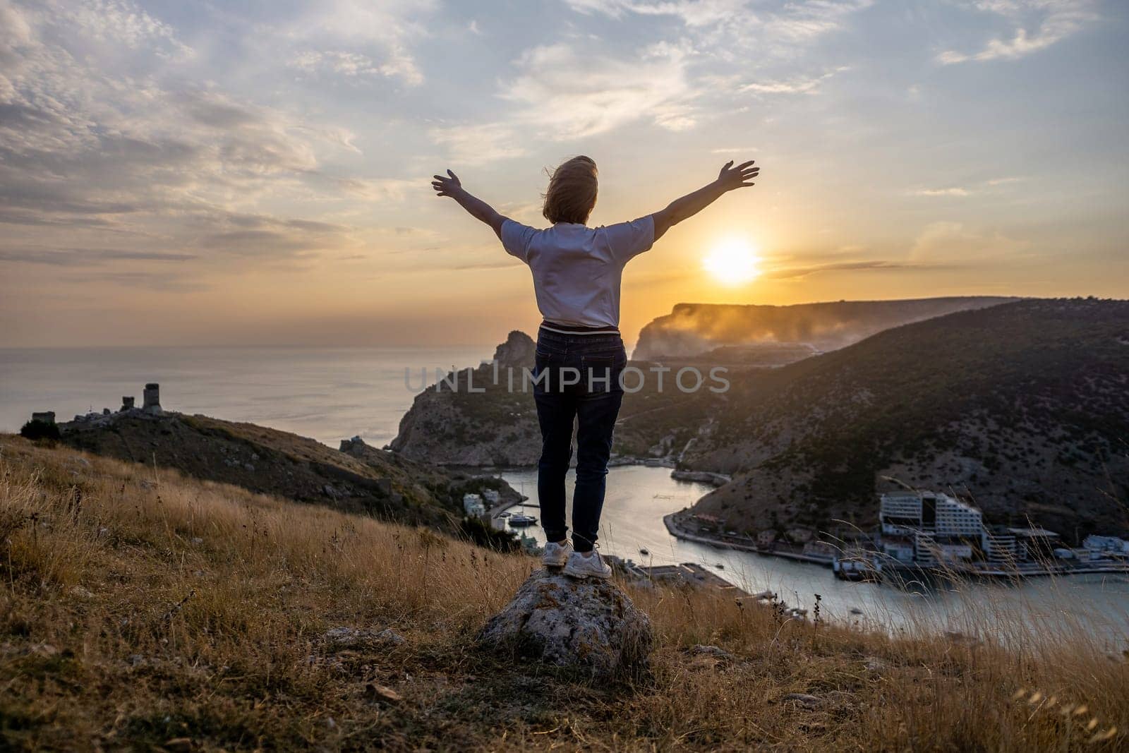 Happy woman on sunset in mountains. Woman standing with her back on the sunset in nature in summer with open hands. Silhouette