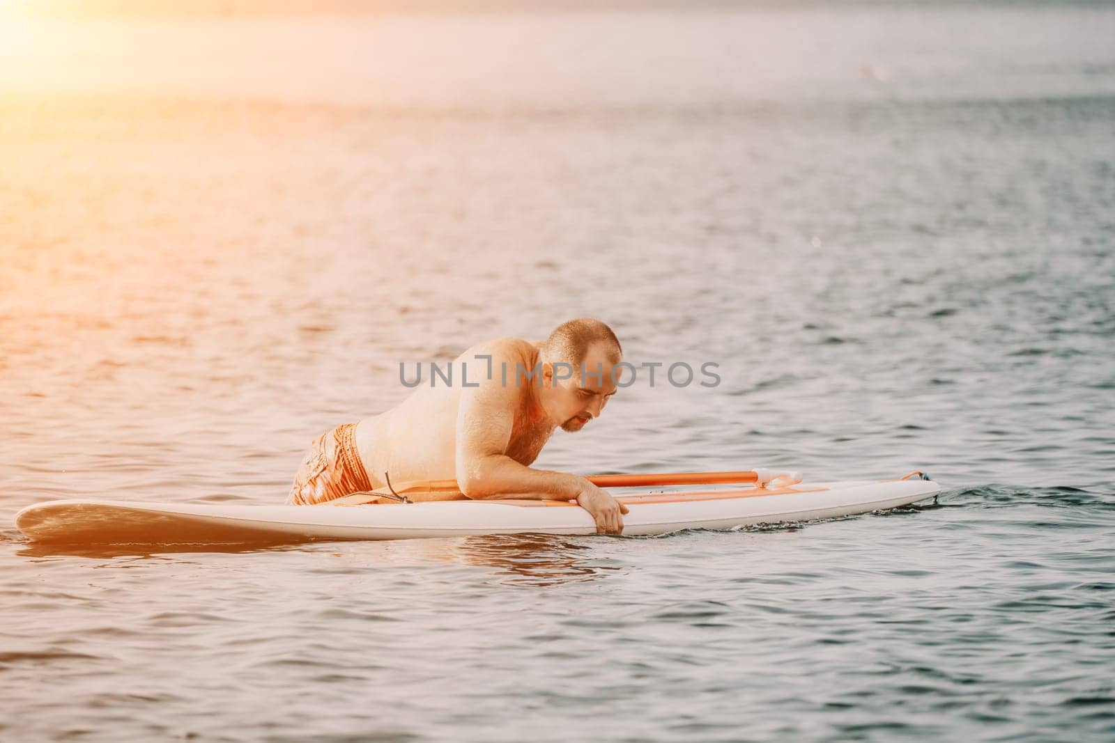 Active mature male paddler with his paddleboard and paddle on a sea at summer. Happy senior man stands with a SUP board. Stand up paddle boarding - outdor active recreation in nature