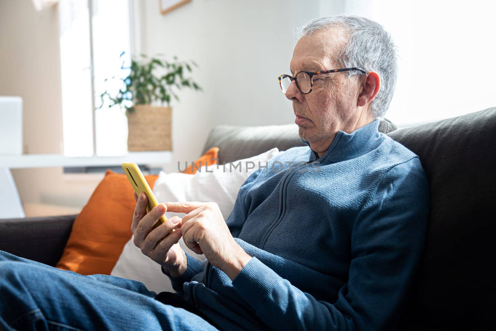 Senior caucasian man using mobile phone sitting on the sofa at home. Lifestyle concept.