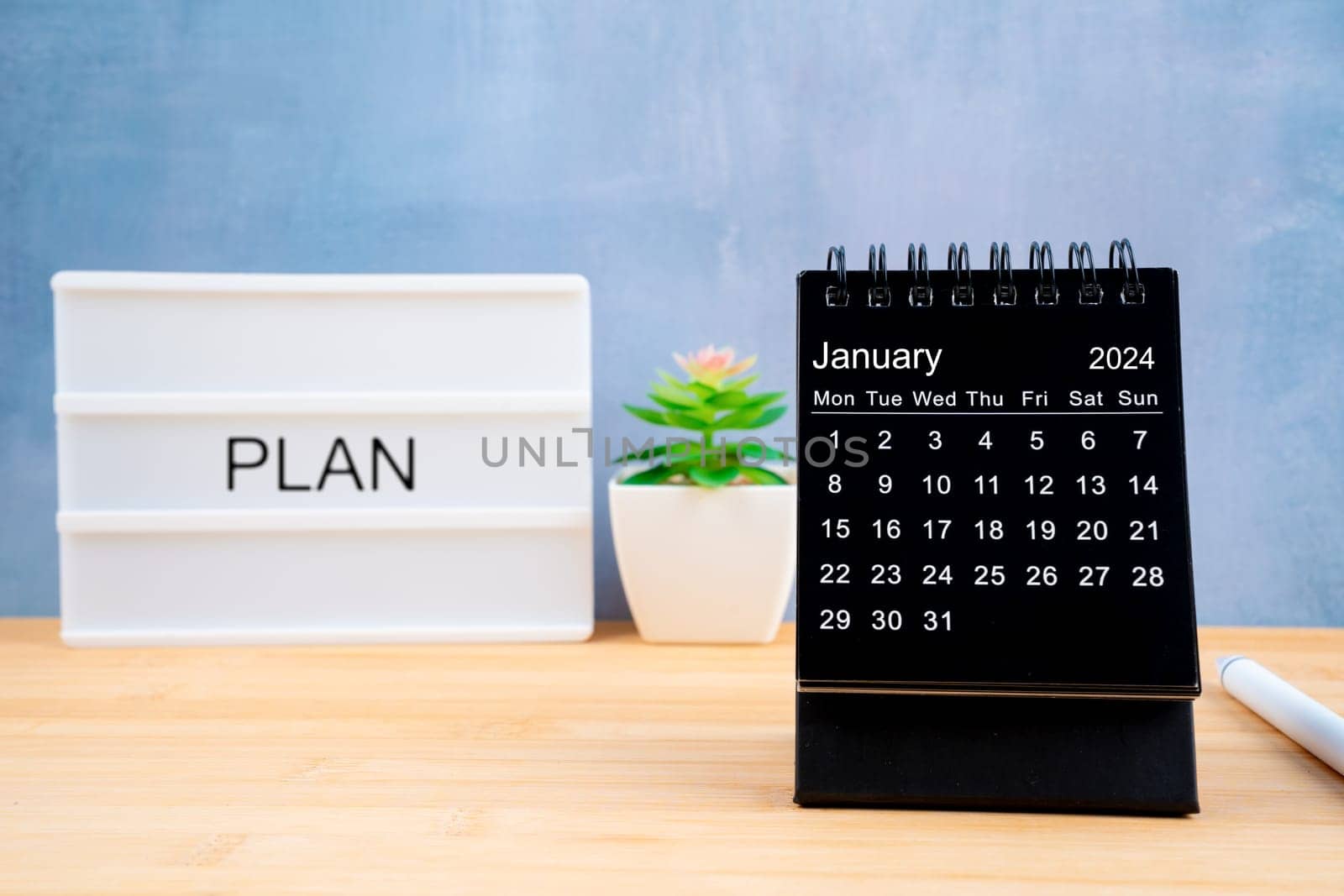 January 2024 black color desk calendar on wooden table with Lightbox displaying by Gamjai