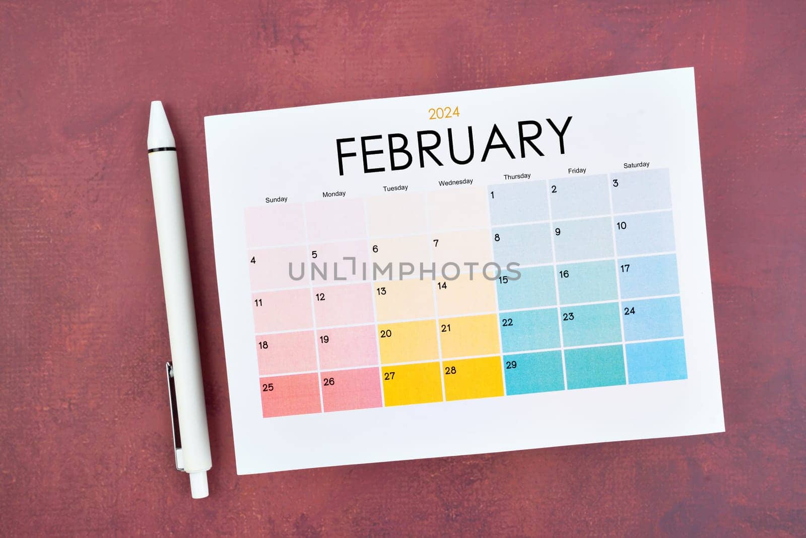 February 2024 calendar page and pen on red color retro background.