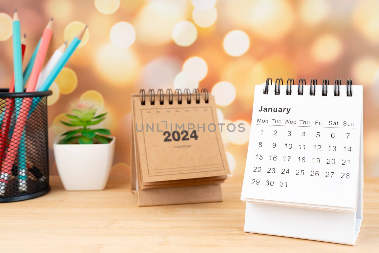 White January 2024 desk calendar on wooden table with gold light bokeh background. New Year Concept.