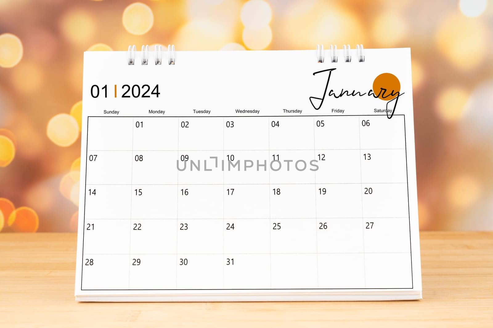 January 2024 desk calendar on wooden table with gold light bokeh background. by Gamjai