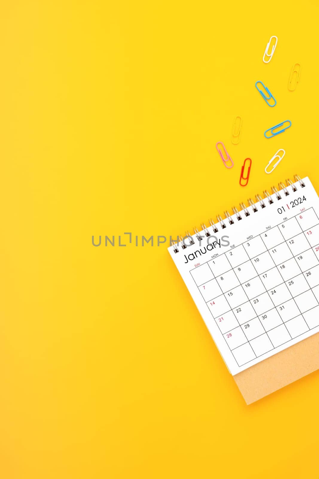 January 2024 desk calendar and paper clips on yellow color background. Position with copy space.