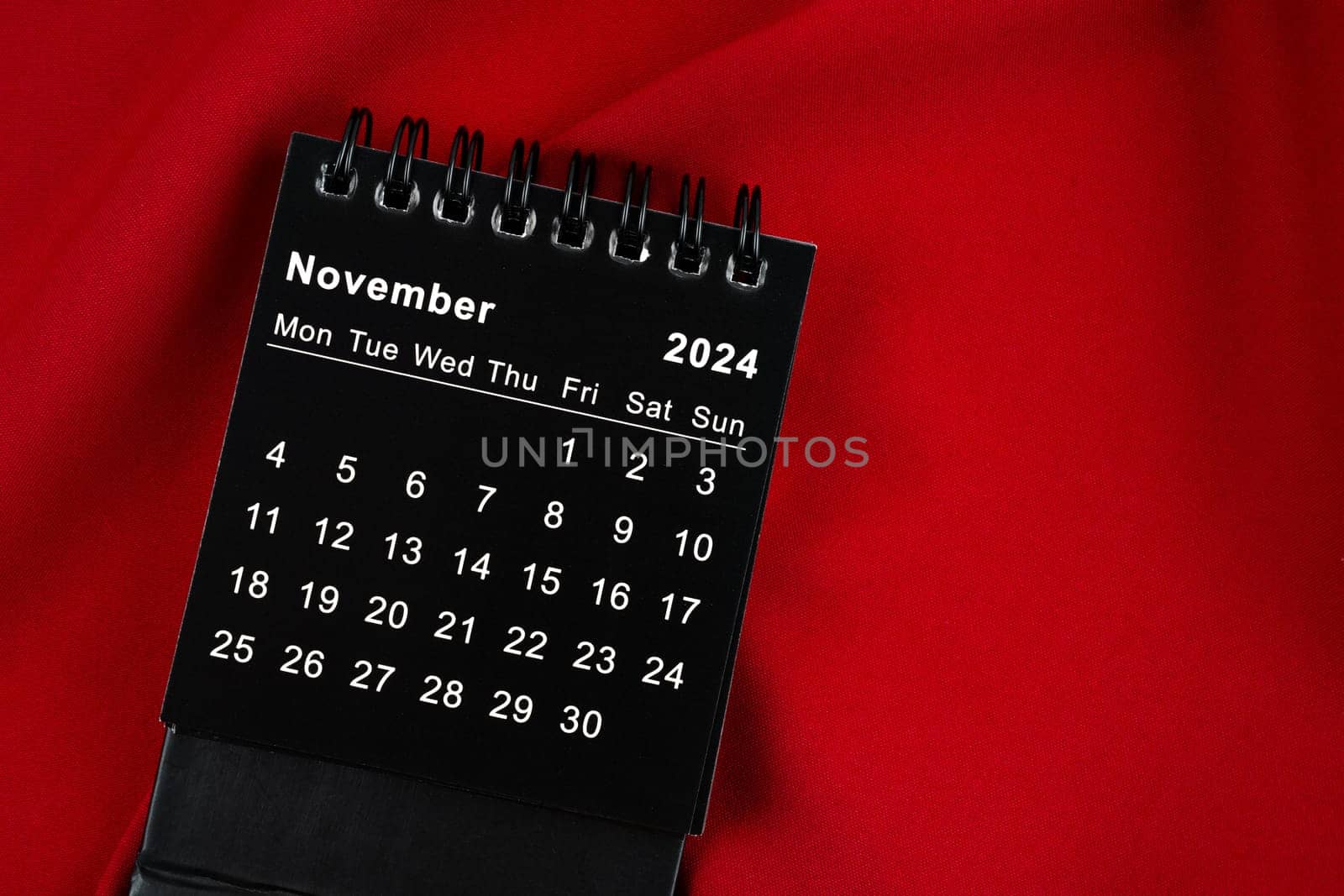 November 2024 Black spiral desktop calendar on red textile.