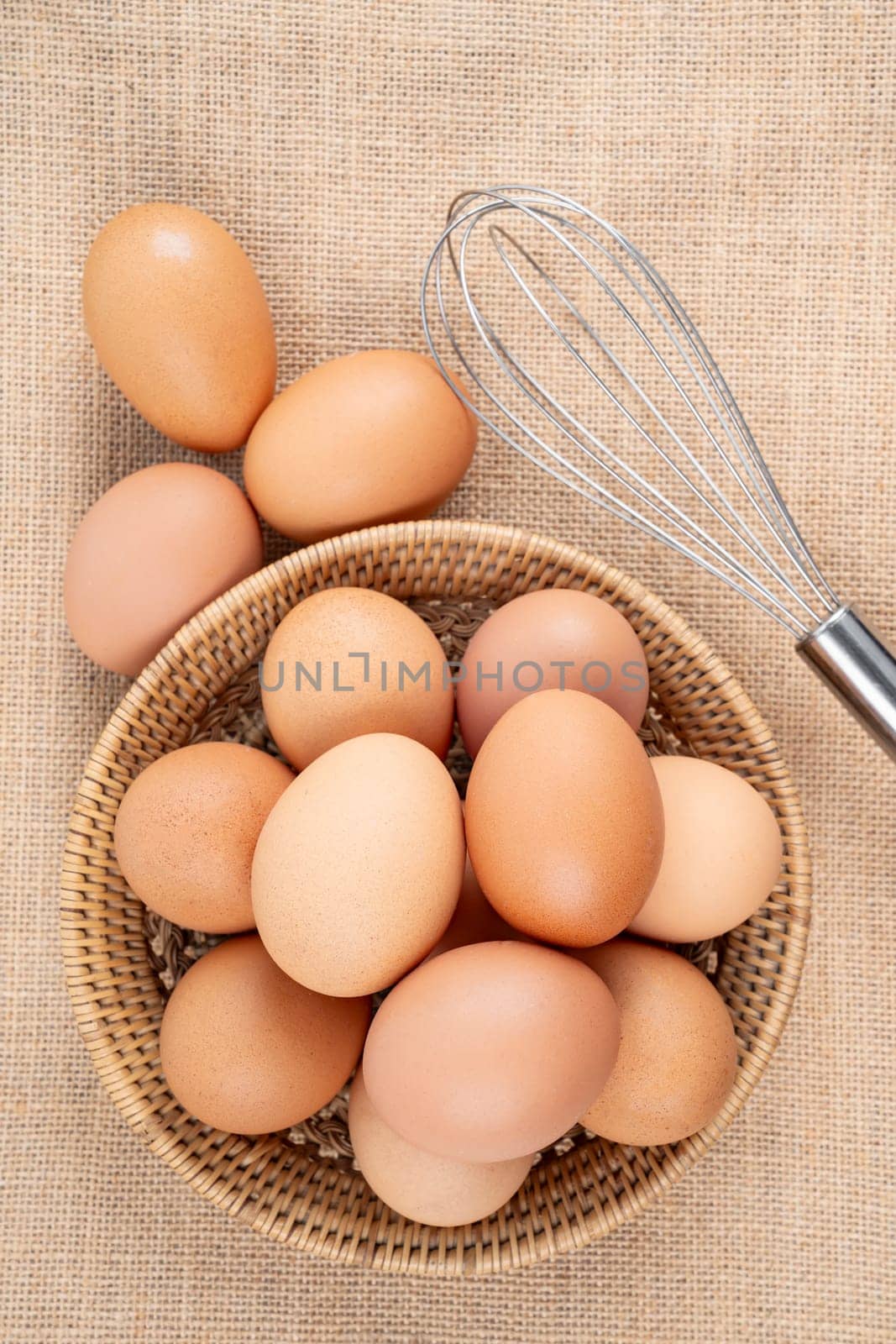 Top view of eggs in a wooden basket and egg whisk. by Gamjai