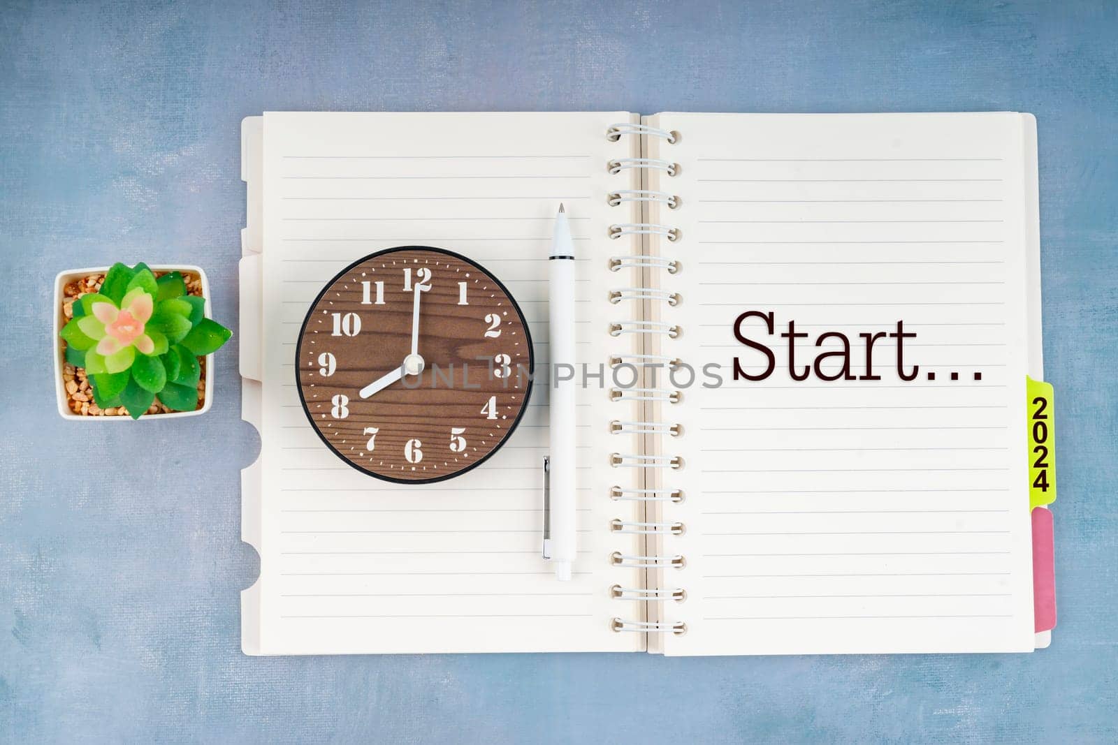 Start 2024 text and wooden clock on open diary. by Gamjai