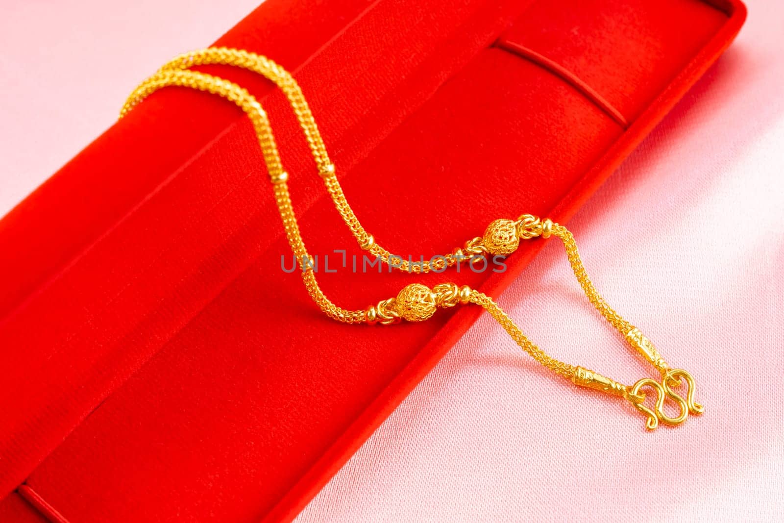 Gold necklace on a red velvet box on a pink color fabric background.