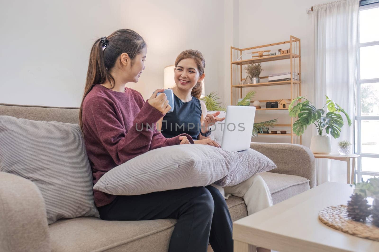 Two women communicate with friends and classmates via video link using laptop and smartphone in living room. Friends, friendship, time together. by wichayada