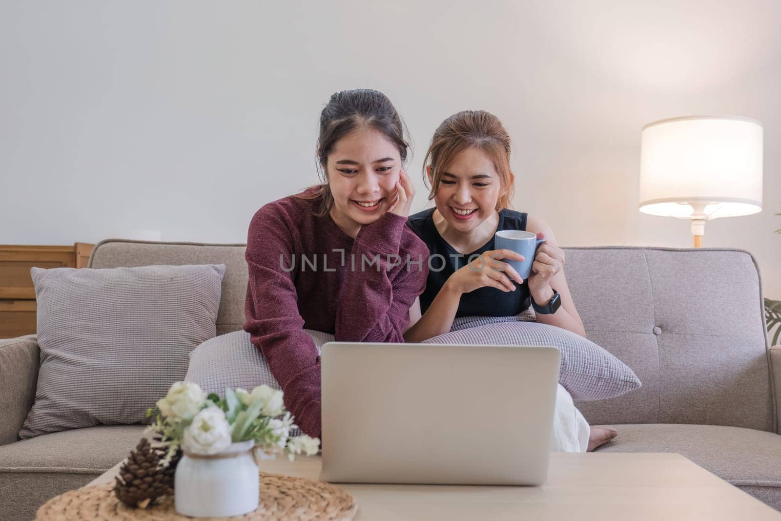 Two women communicate with friends and classmates via video link using laptop and smartphone in living room. Friends, friendship, time together. by wichayada