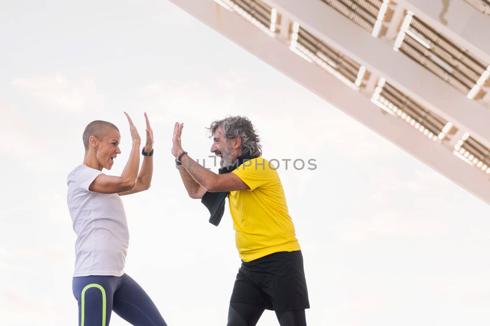senior sports man and his personal trainer smiling happily high five with joy after a training session, concept of active and healthy lifestyle in the middle age, copy space for text