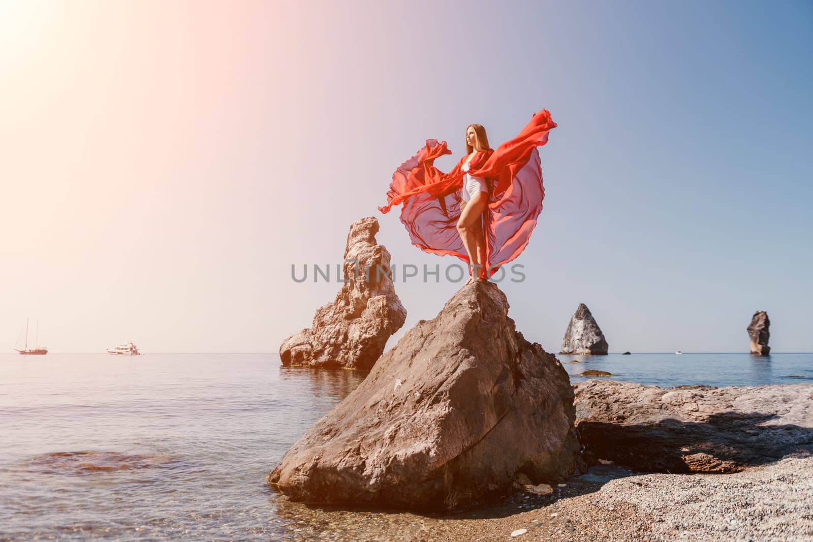 Woman travel sea. Young Happy woman in a long red dress posing on a beach near the sea on background of volcanic rocks, like in Iceland, sharing travel adventure journey by panophotograph