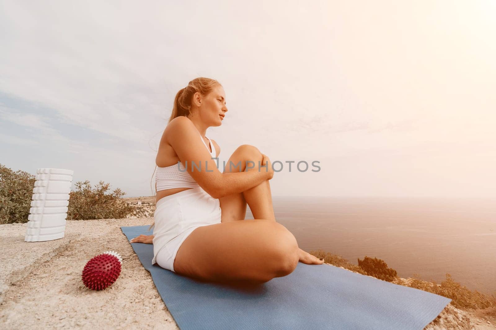 Middle aged well looking woman with black hair doing Pilates with the ring on the yoga mat near the sea on the pebble beach. Female fitness yoga concept. Healthy lifestyle, harmony and meditation.