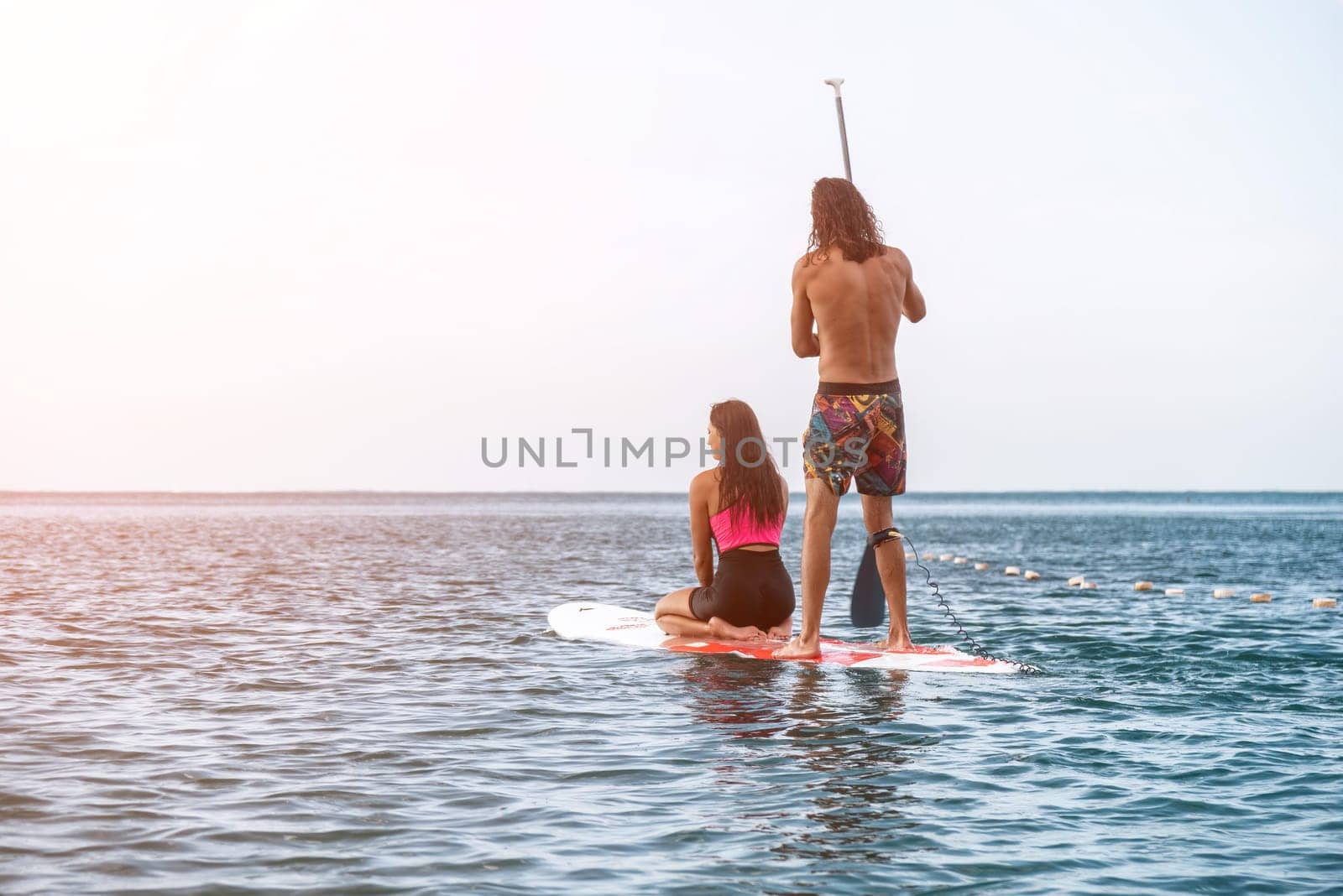 Sea woman and man on sup. Silhouette of happy young woman and man, surfing on SUP board, confident paddling through water surface. Idyllic sunset. Active lifestyle at sea or river