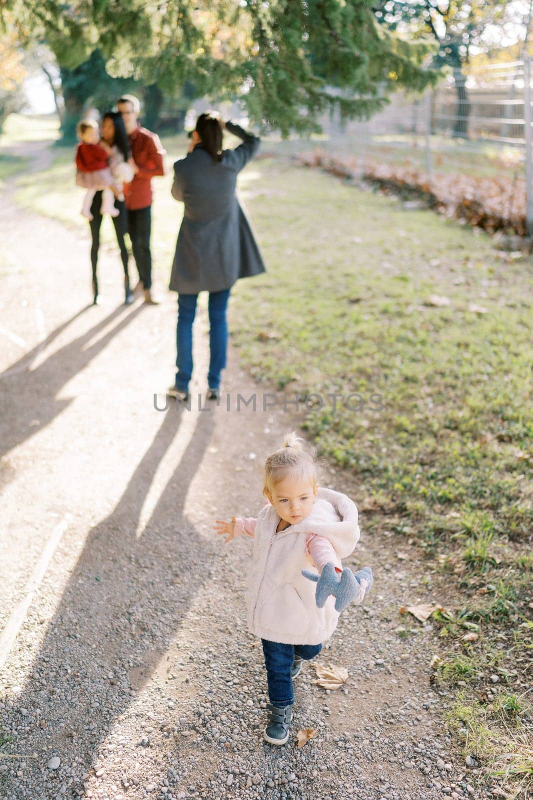 Little girl is standing on a path against the background of a photographer taking pictures of a married couple with a child. High quality photo