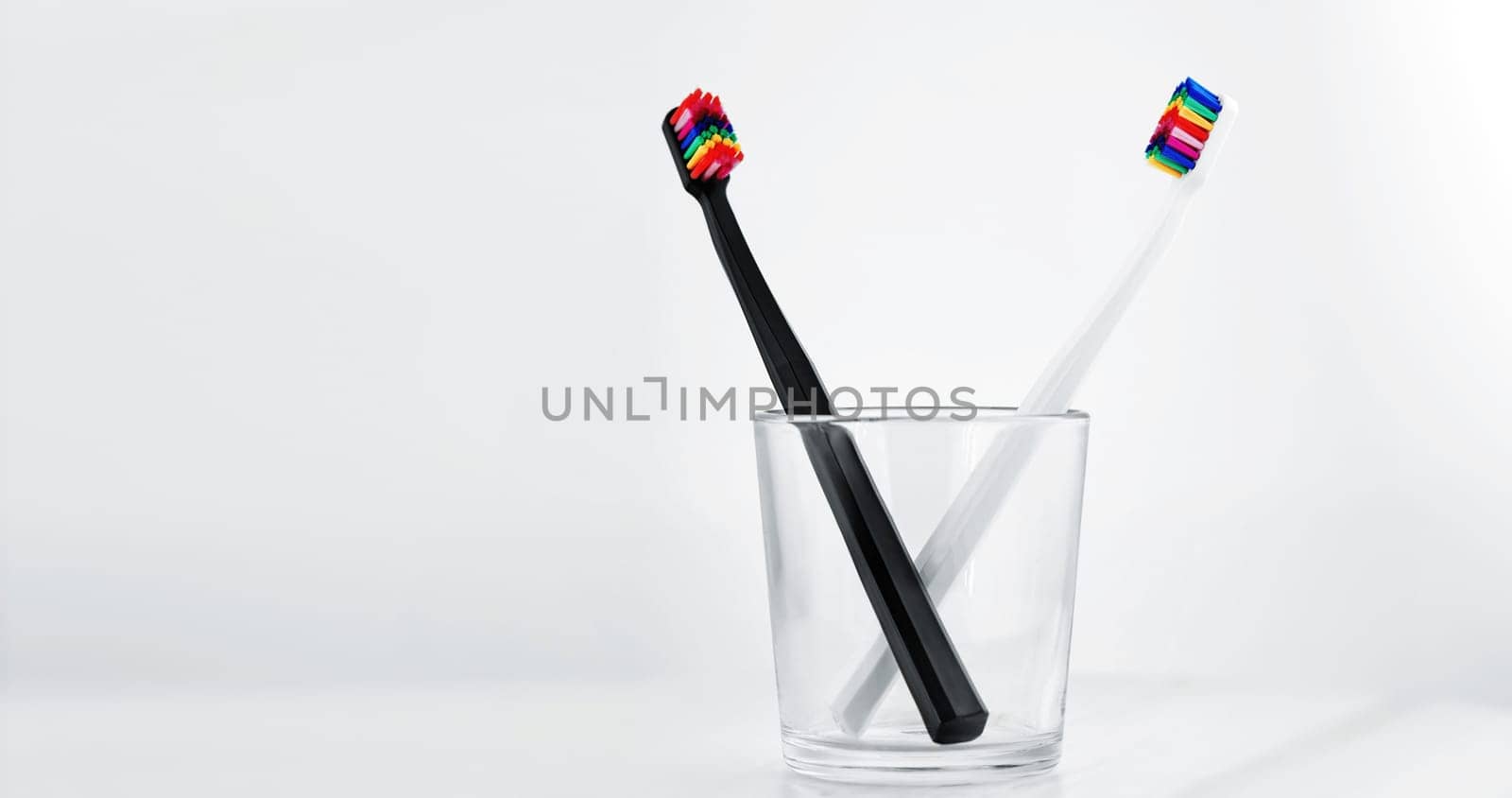 Stylish dental abacus in a glass cup. Black and White toothbrushs with multicolored bristles on white background. Bristles in all colors of the rainbow. Rainbow toothbrush Fashionable oral care.