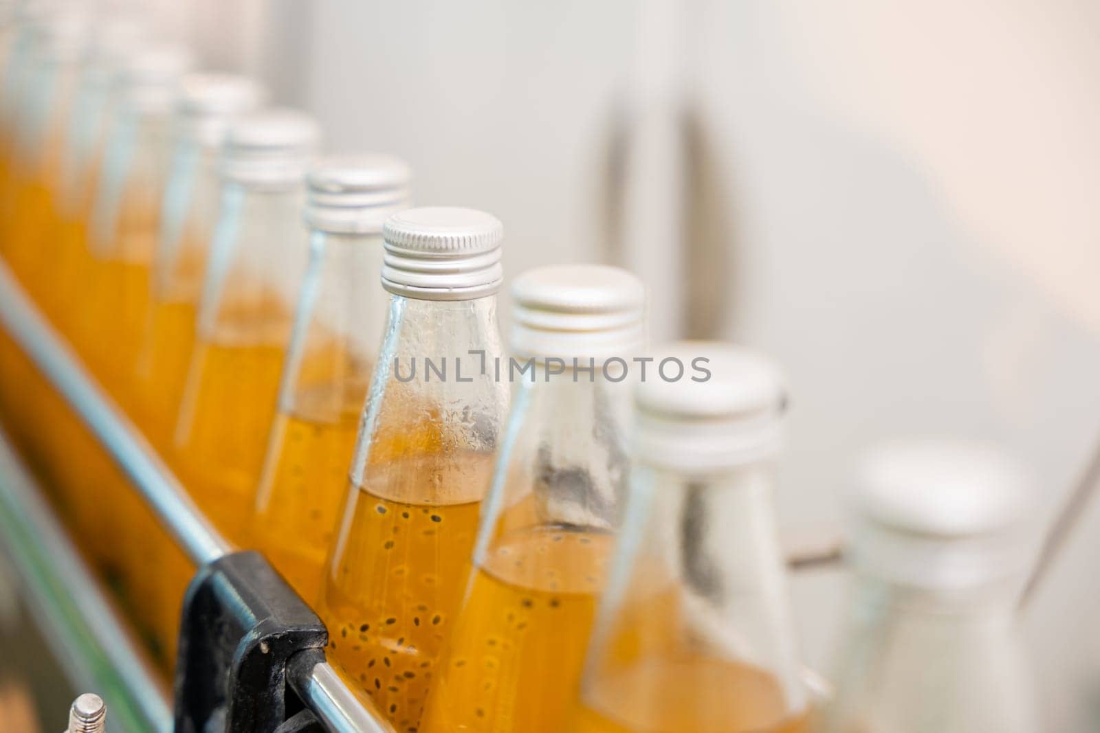 Factory's clean automated process fills transparent bottles with organic basil or chia seed drinks mixed with pomegranate. High-quality manufacturing is evident in the outcome.