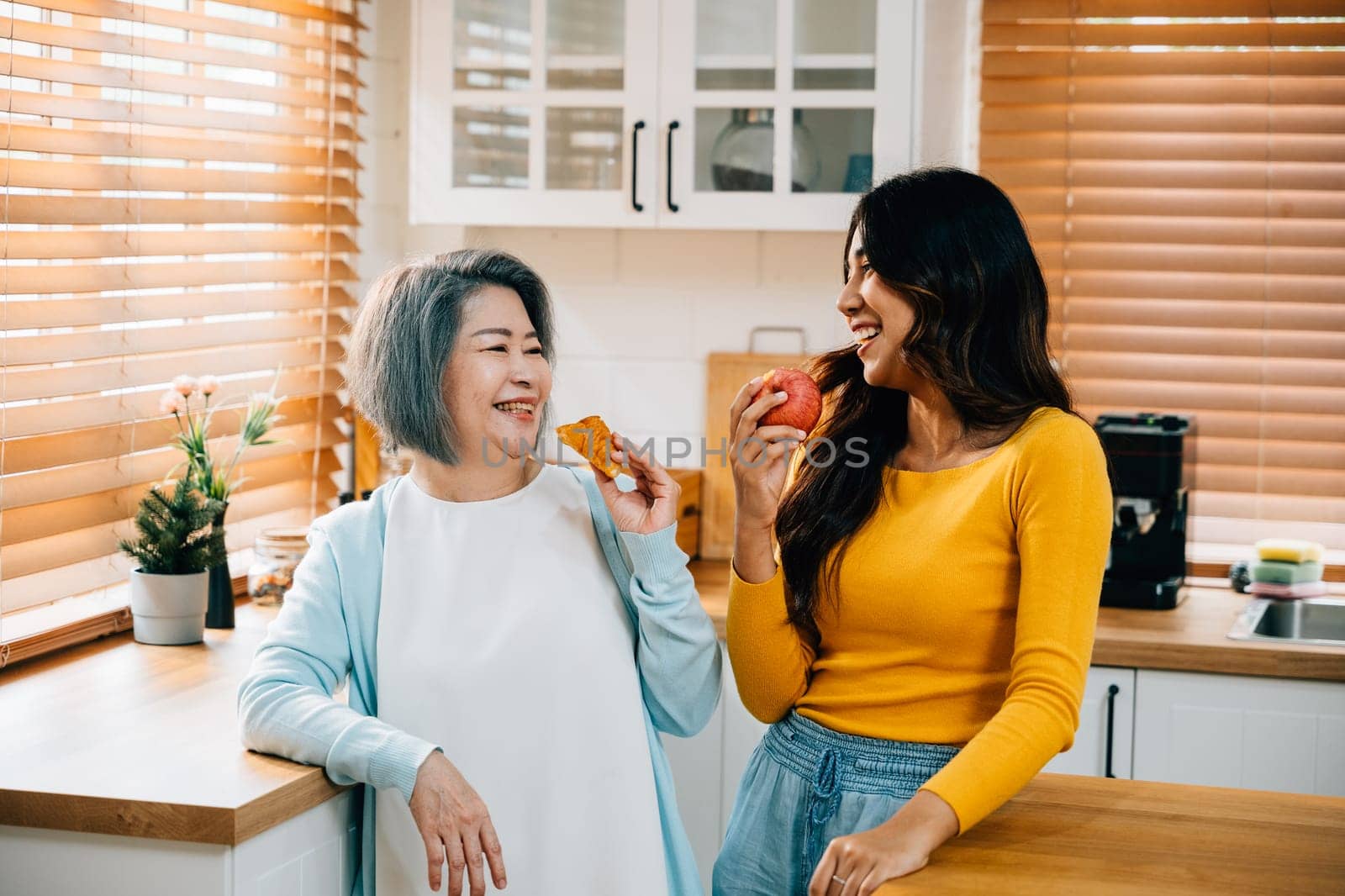 At home, an old mother and her daughter, a young woman, share quality time in the kitchen. The daughter is assisting her mother, creating a heartwarming portrait of family togetherness and care. by Sorapop
